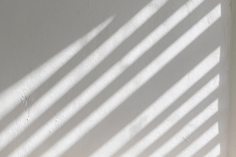Diagonal light streaks cast on a white plaster wall indoors