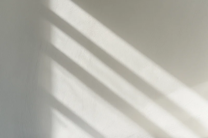 Diagonal light and shadow stripes on a white plaster wall interior