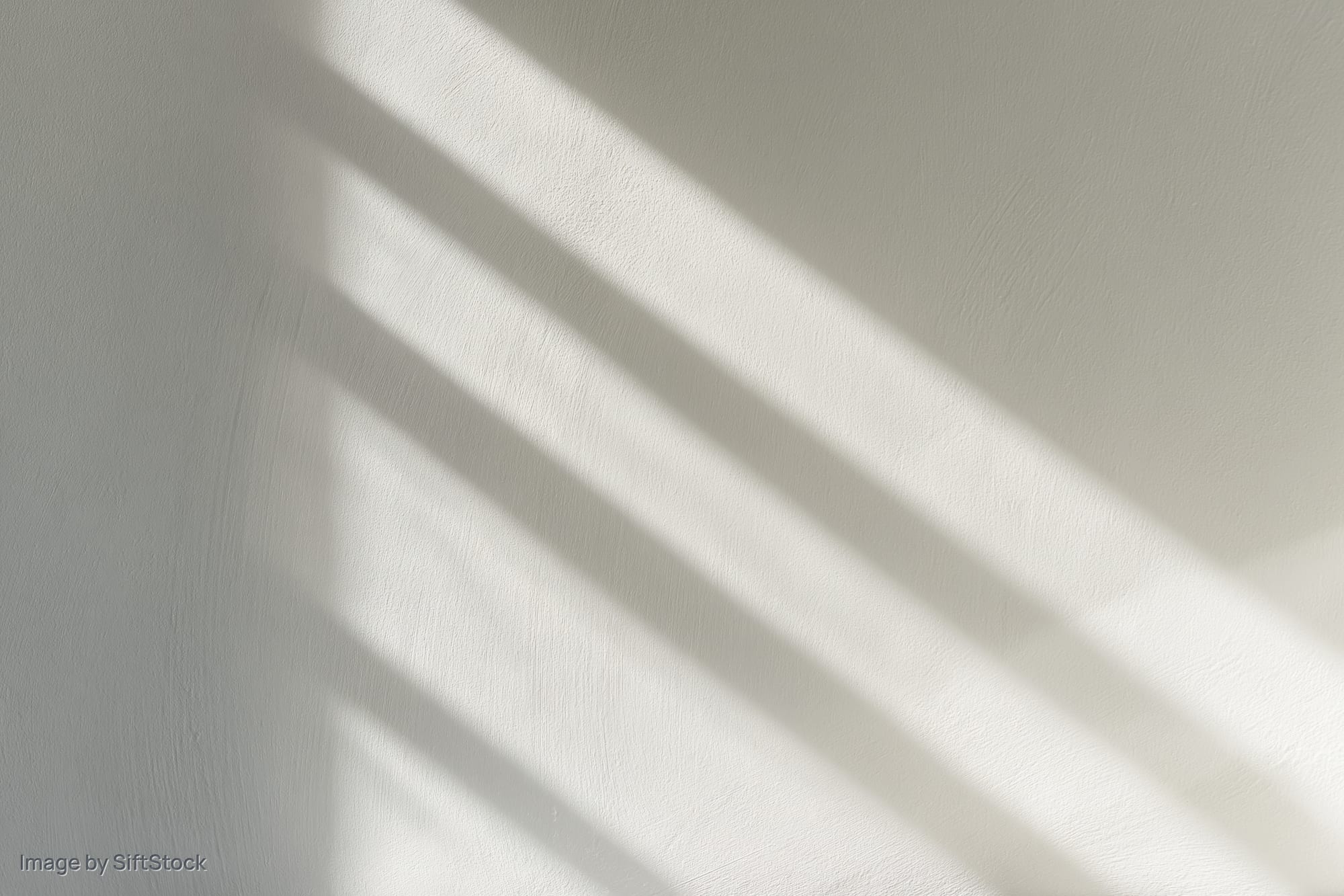 Diagonal light and shadow stripes on a white plaster wall interior