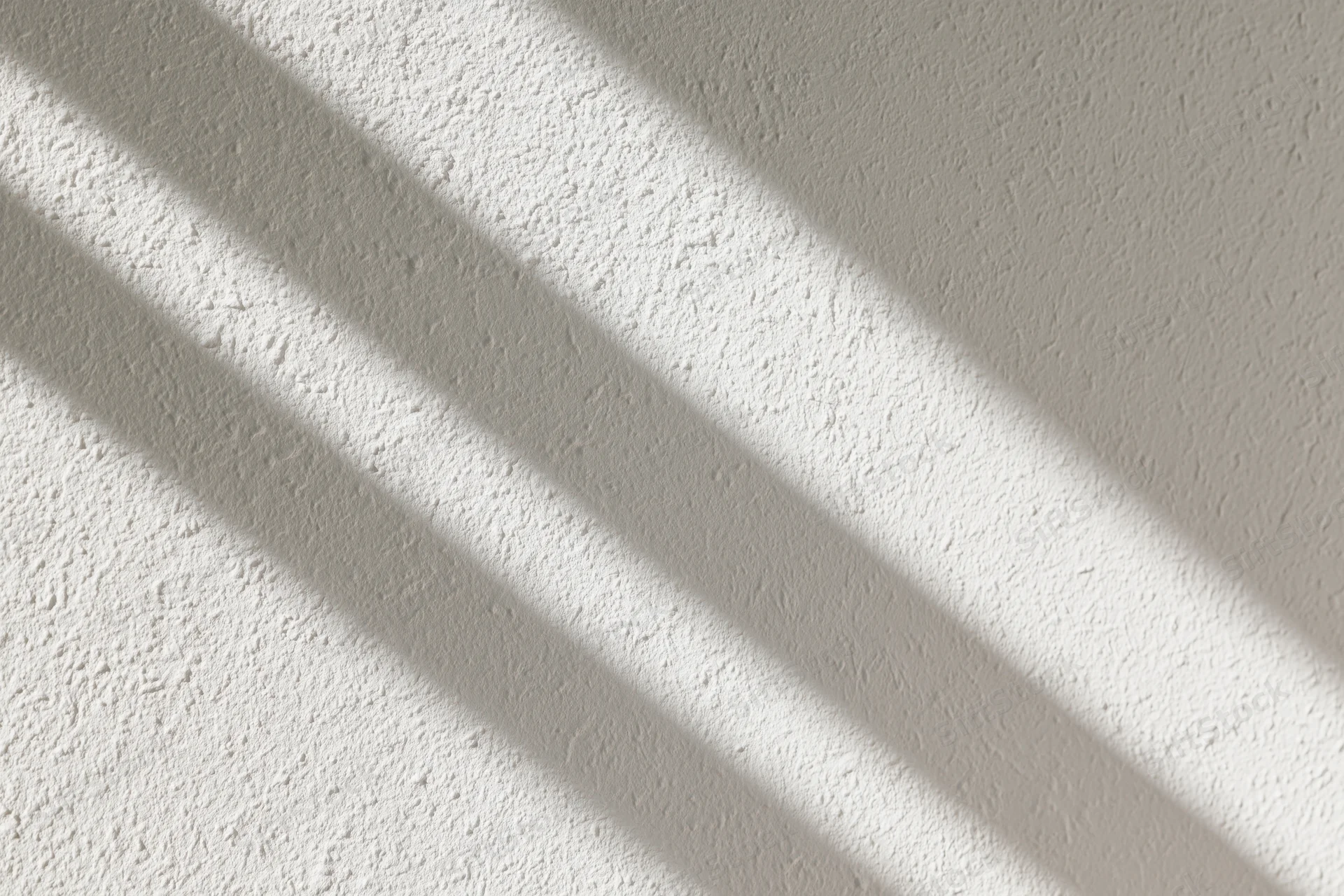 Diagonal shadows cast on a textured white plaster wall in an interior space