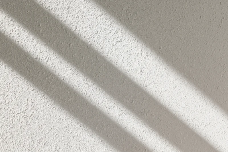 Diagonal shadows cast on a textured white plaster wall in an interior space