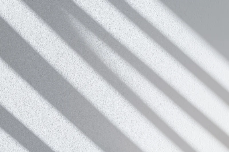 Diagonal shadows from window blinds on a textured white wall