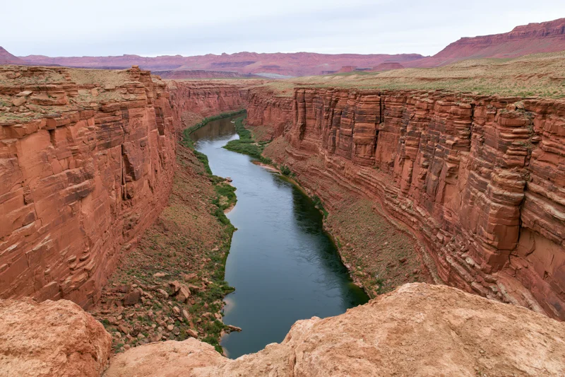 Wide aerial view of a deep red rock canyon with a winding river through arid desert landscape