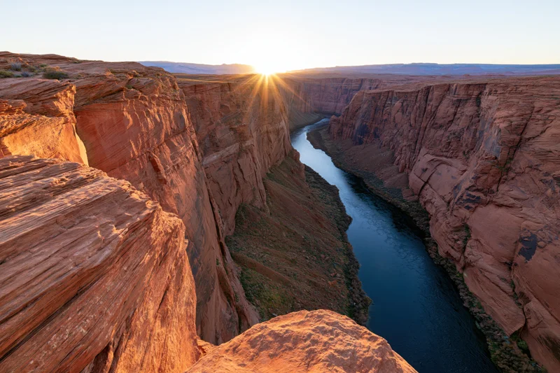 Wide view from canyon rim overlooking river winding through red rock gorge at sunset