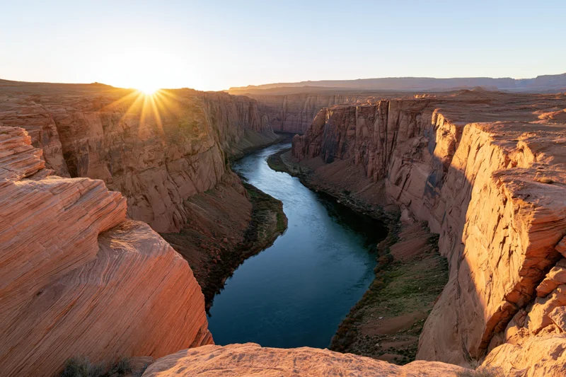 Wide view from canyon rim overlooking river winding through red rock cliffs at sunset