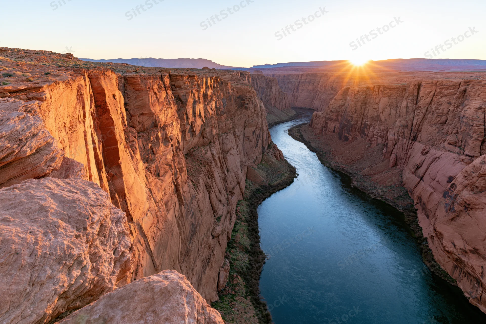 Wide view of a deep canyon with a winding river at sunset from the rim