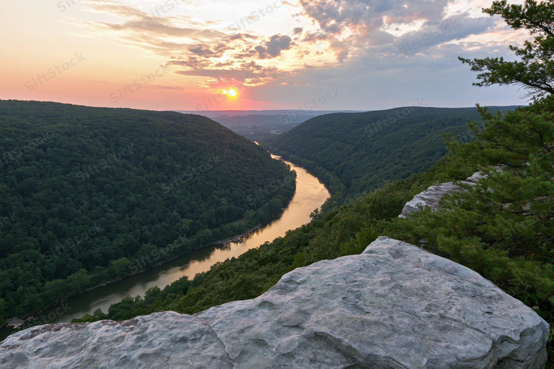 Wide view from rocky overlook overlooking winding river through forested valley at sunset