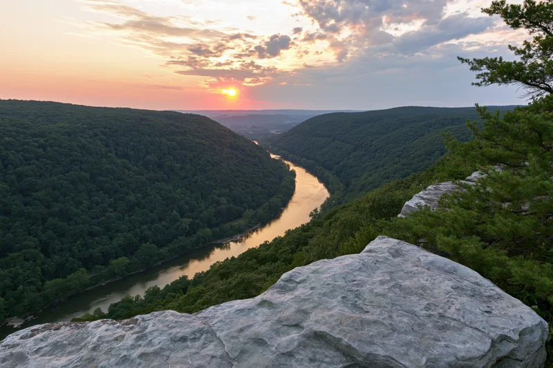 Wide view from rocky overlook overlooking winding river through forested valley at sunset
