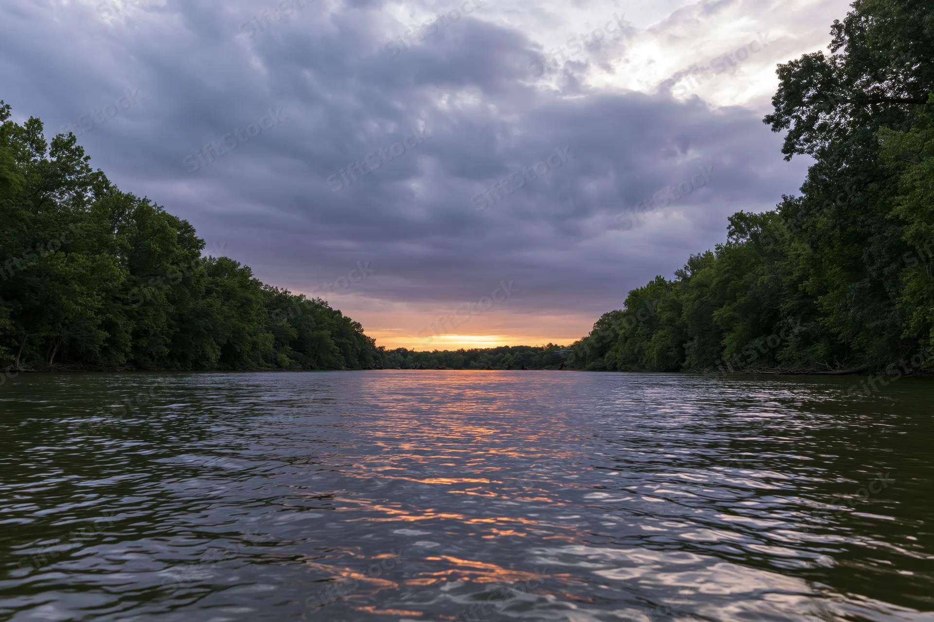 Wide river at dusk with trees on both banks reflecting sunset light