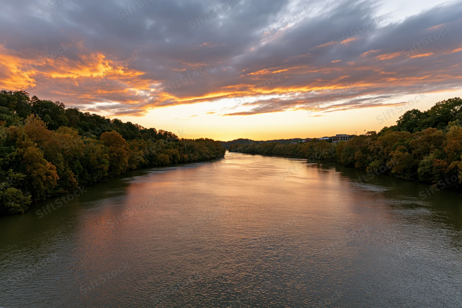 Wide river reflecting golden sunset sky flanked by autumn trees