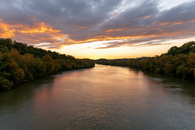 Wide river reflecting golden sunset sky flanked by autumn trees