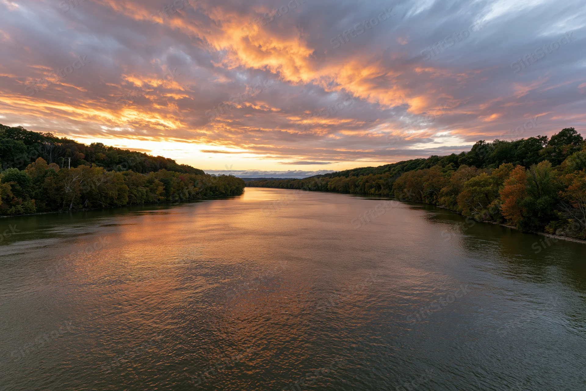 Wide river reflecting golden sunset sky flanked by autumn trees