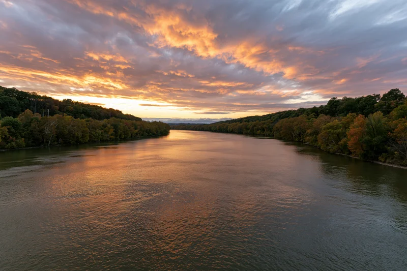 Wide river reflecting golden sunset sky flanked by autumn trees