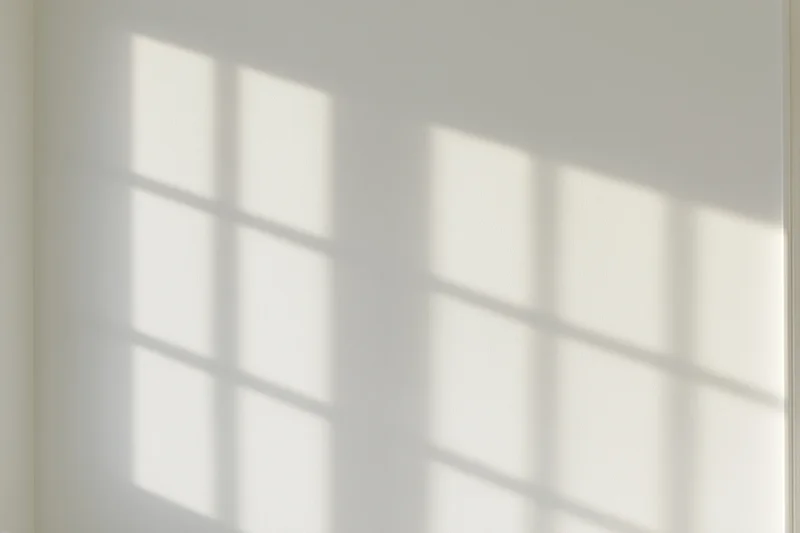 Grid shadow from a window cast across a plain white interior wall
