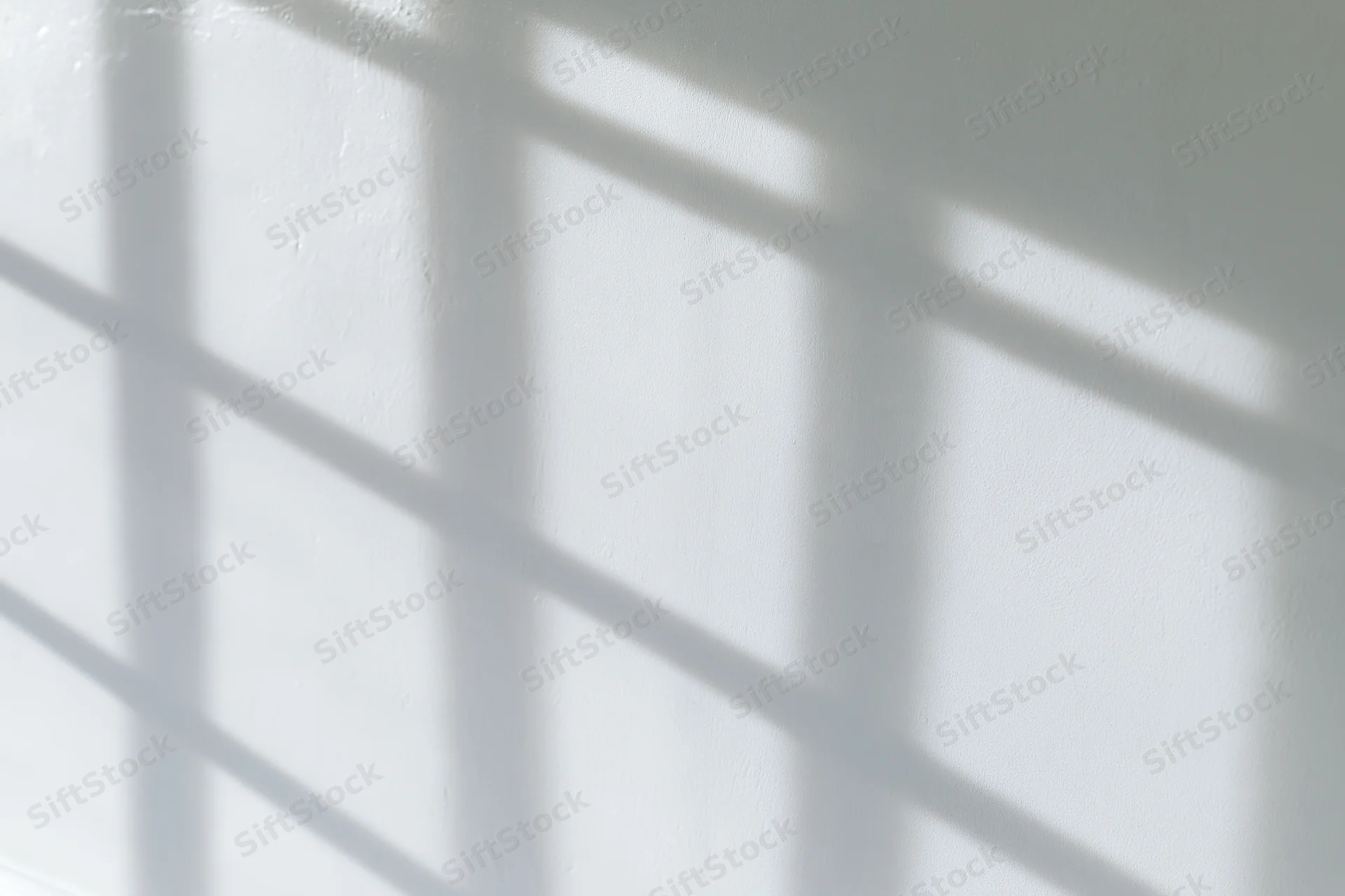 Grid shadow pattern from window light on white wall interior