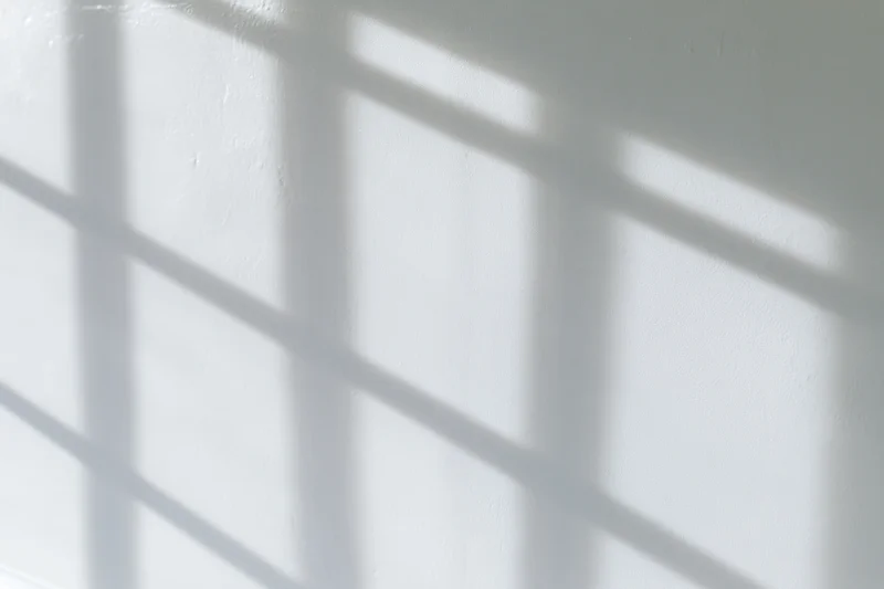 Grid shadow pattern from window light on white wall interior
