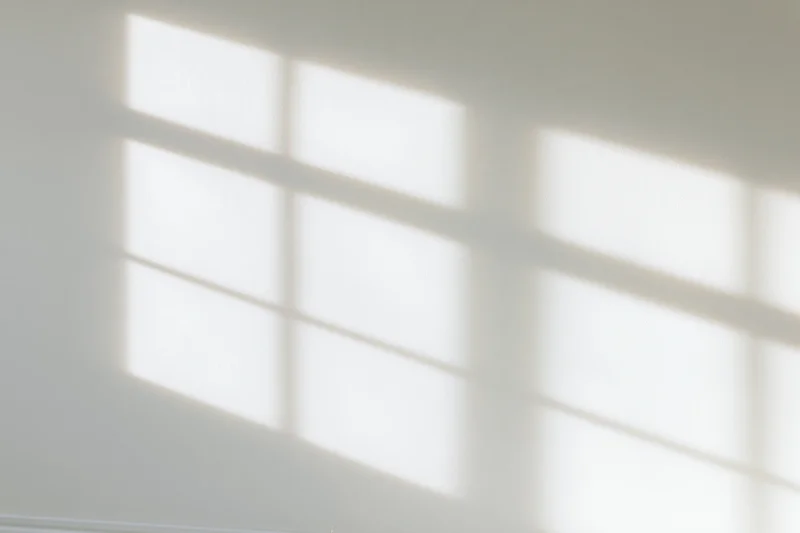 Shadow pattern from window blinds cast across a white interior wall