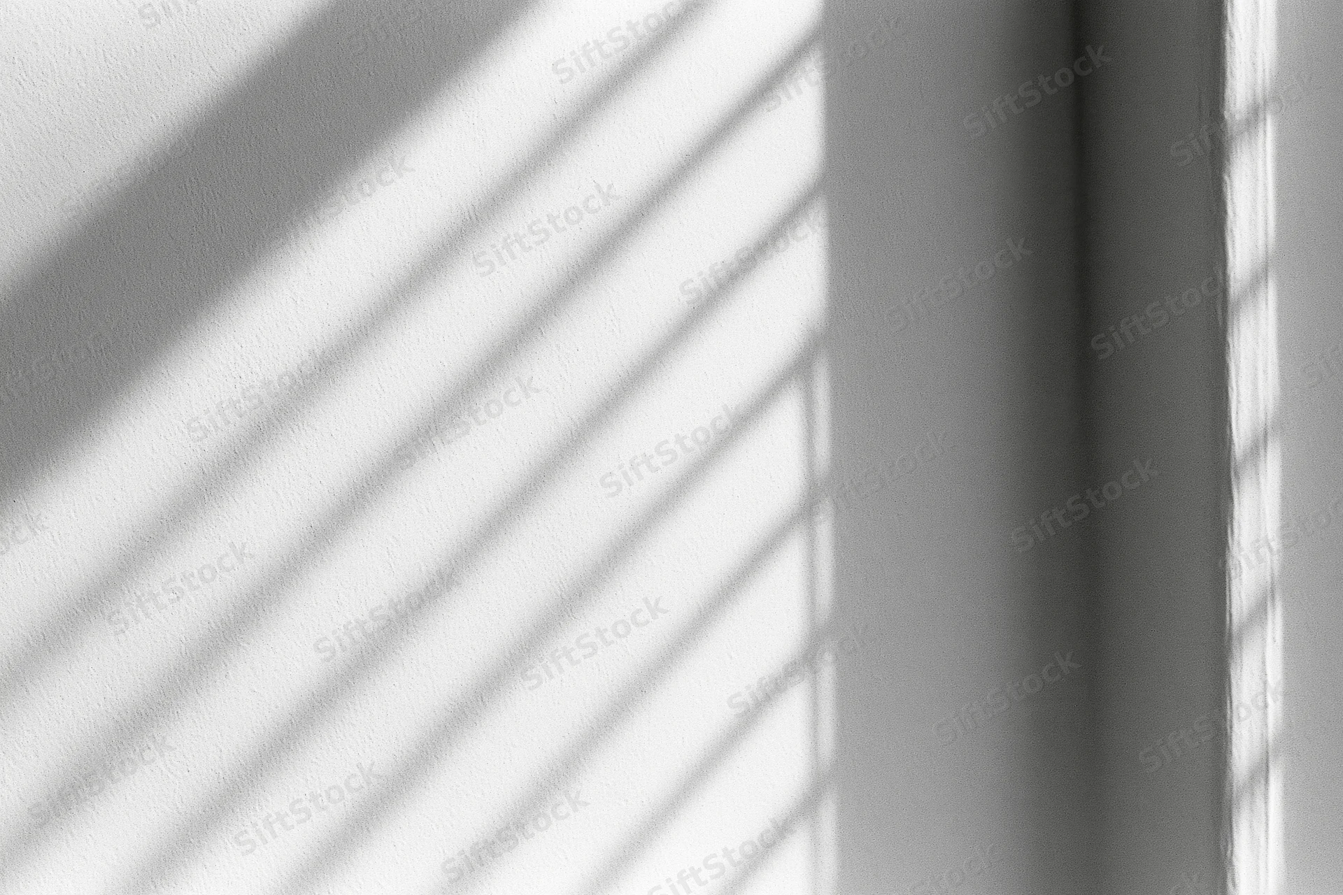 Diagonal shadow stripes from window blinds cast across a white interior wall