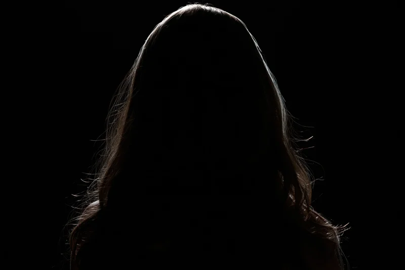 Silhouette of a woman with long hair facing away from the camera against a dark background
