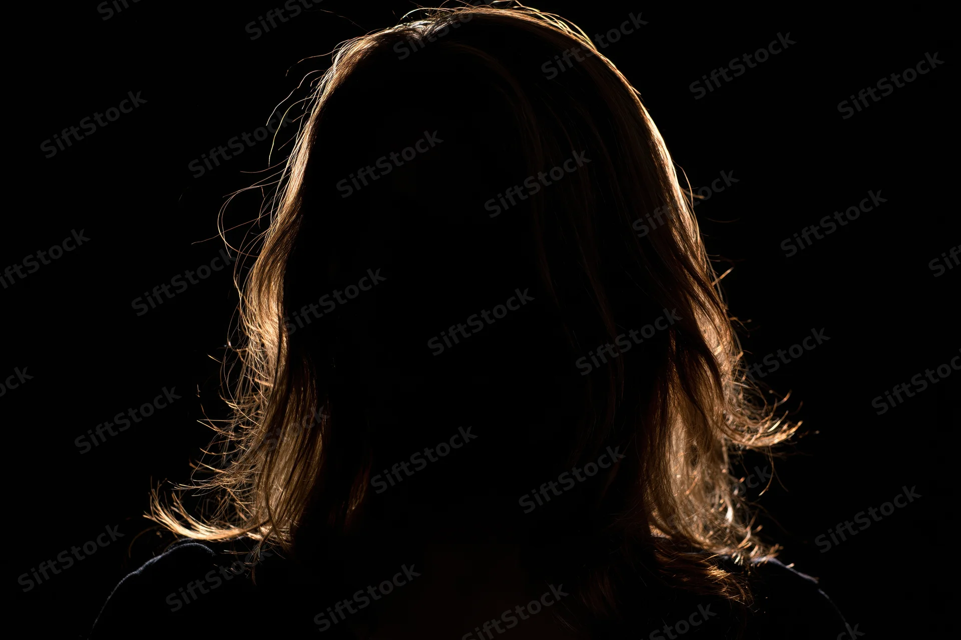 Woman in silhouette with backlit hair against black background