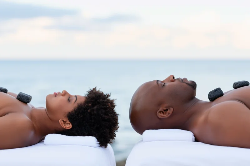 Black couple lying face up on massage tables with hot stones on their backs by the ocean