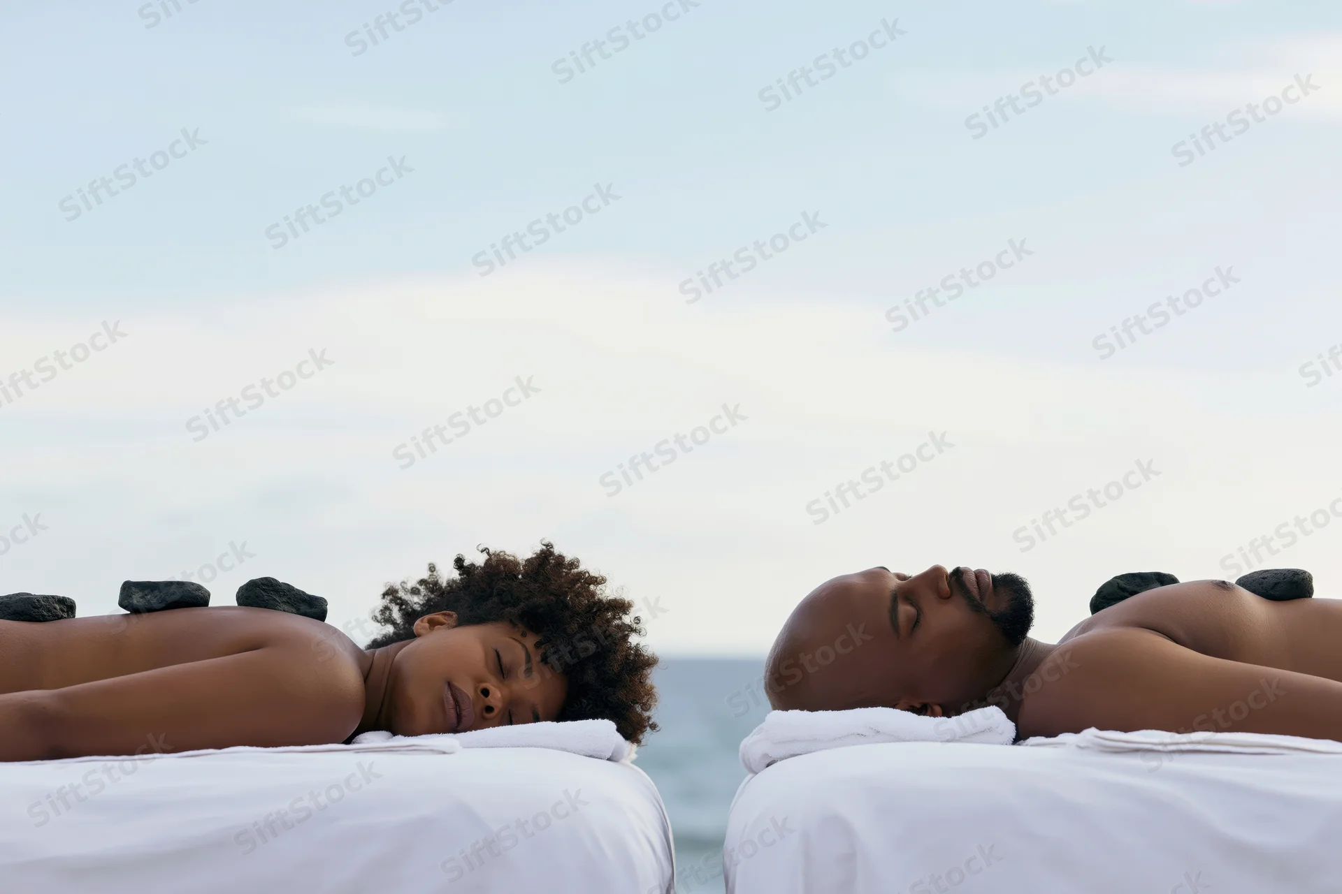 Black couple lying face down on massage tables with hot stones on their backs by the ocean