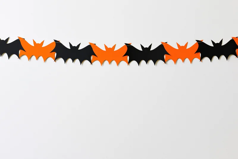 Alternating black and orange paper bat cutouts strung as a garland across a white wall
