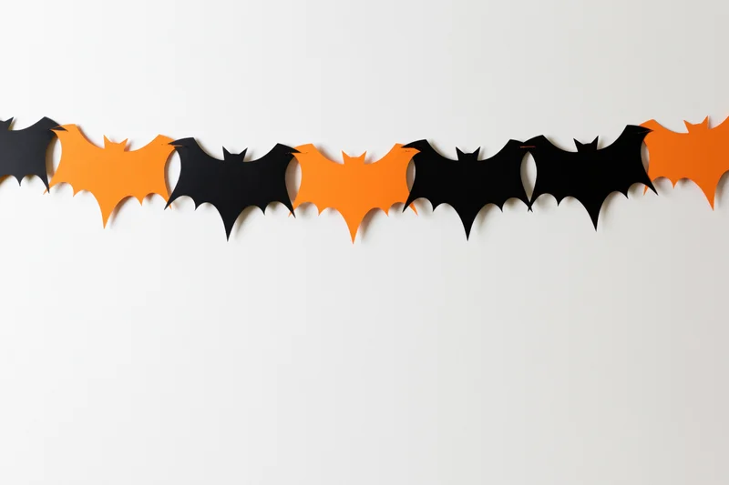 Alternating black and orange paper bat cutouts strung as a garland on a white wall