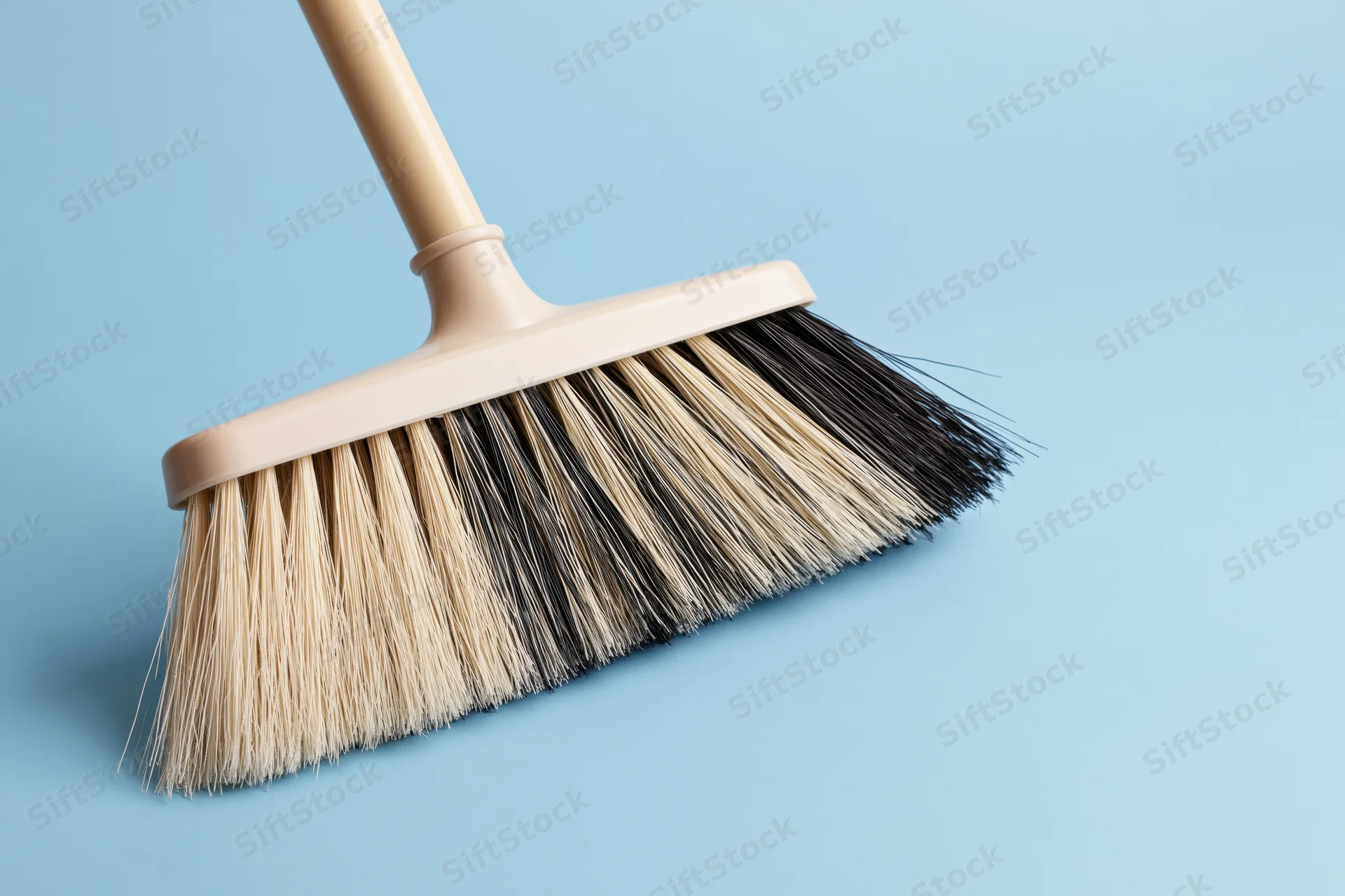 Beige plastic broom with mixed black and cream bristles on a light blue background