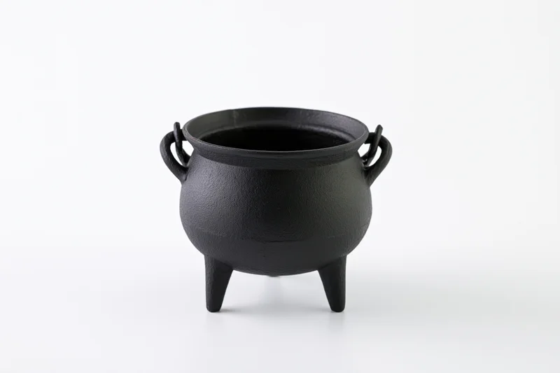 Black cast iron cauldron with three legs and two handles on white background