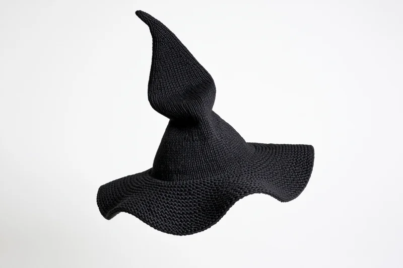 Black knitted witch hat with tall pointed peak floating against white background