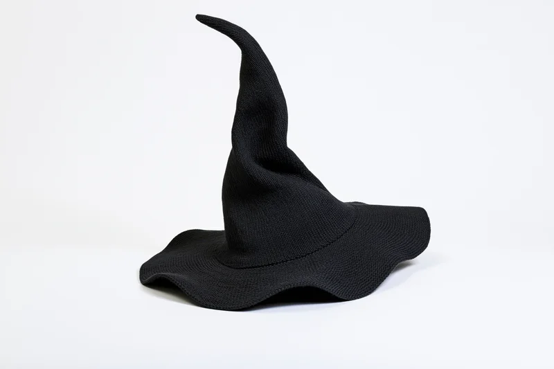 Black knitted witch hat with tall pointed peak on white background