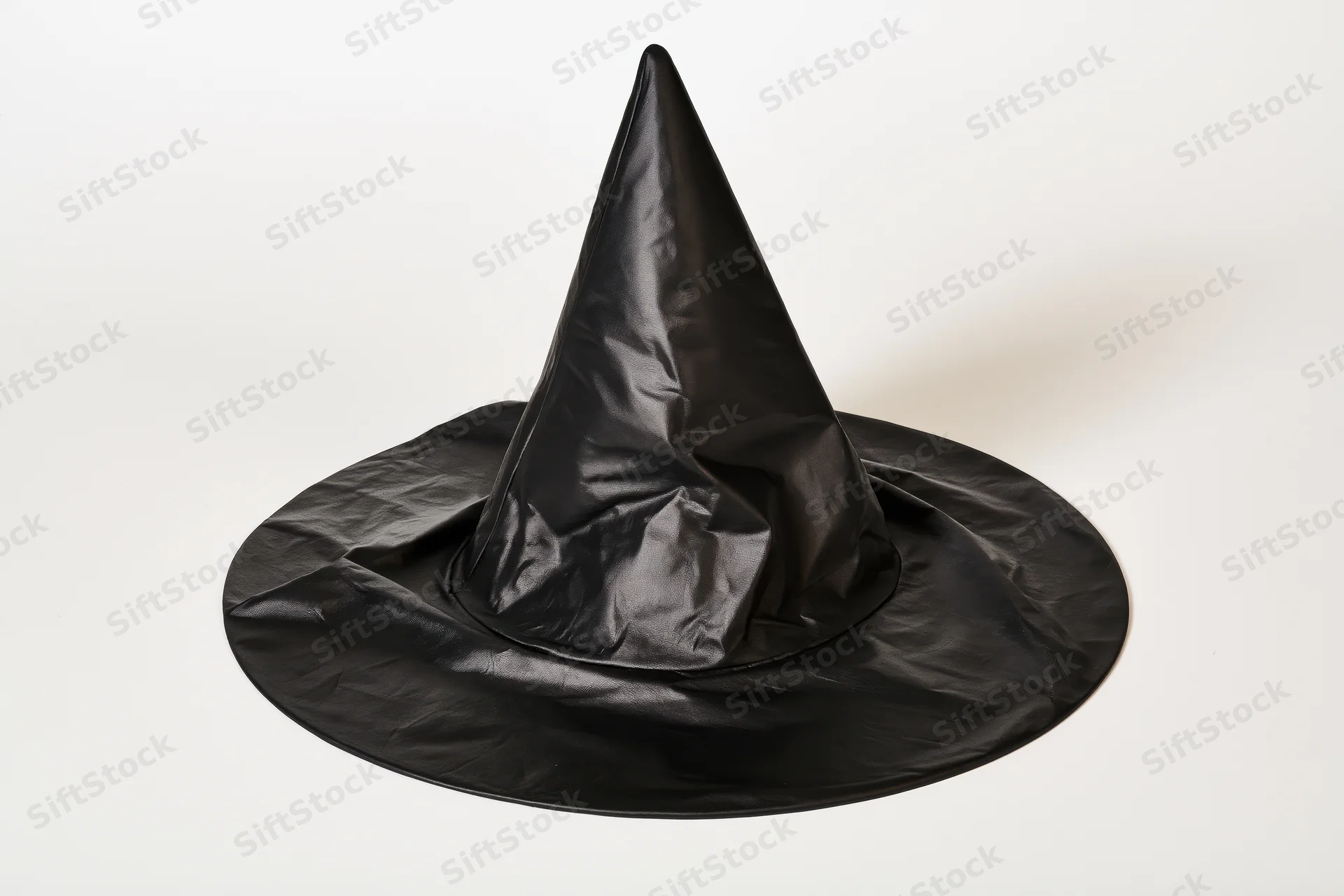 Black plastic witch hat with pointed cone and wide brim lying slightly tilted on white background