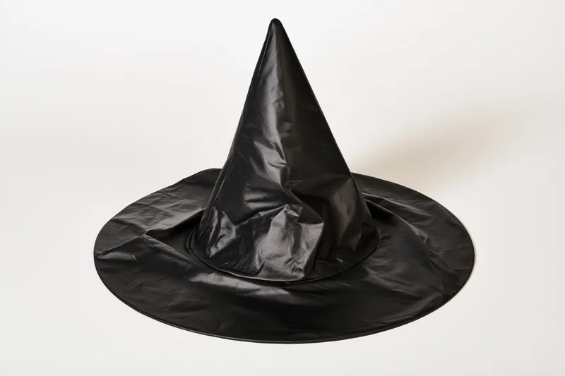 Black plastic witch hat with pointed cone and wide brim lying slightly tilted on white background