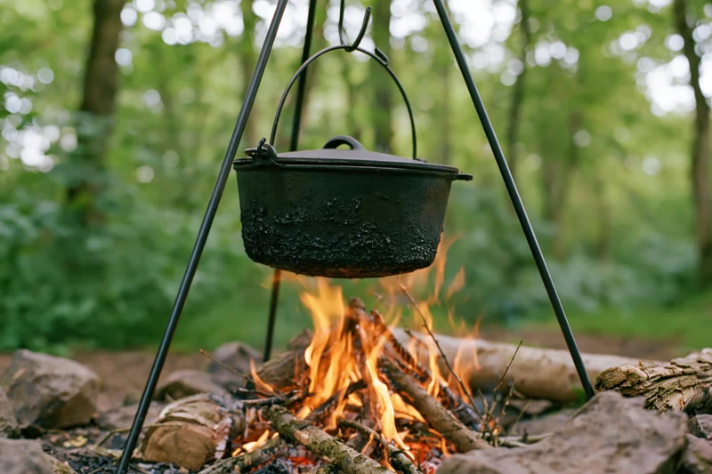 Blackened cast iron pot hanging over a campfire in a forest clearing