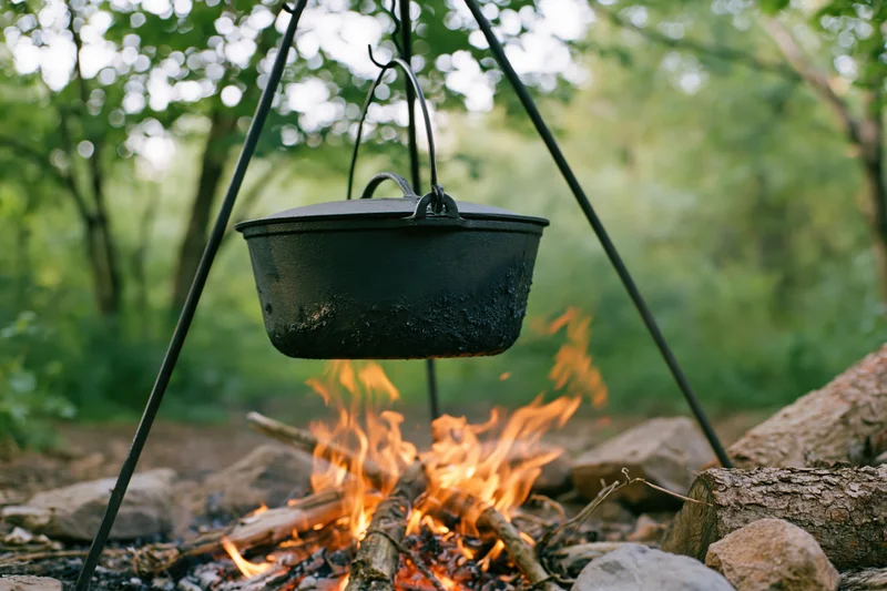 Blackened cast iron pot hanging over a campfire in a forest clearing