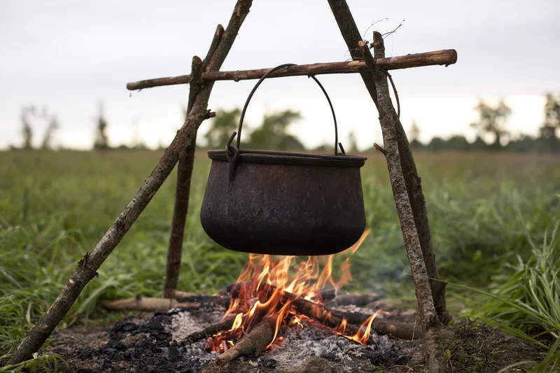 Blackened cast iron pot hanging over a campfire in a grassy field