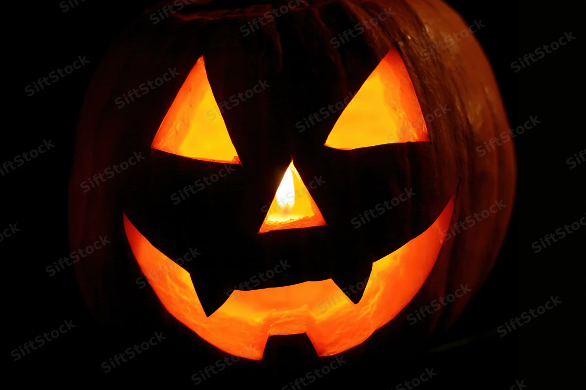 Carved pumpkin with triangular eyes nose and jagged mouth glowing from within at night