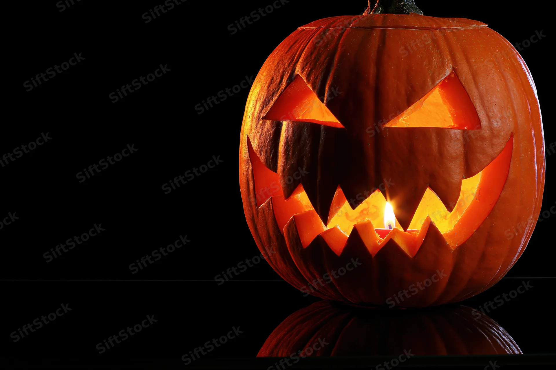 Carved pumpkin with glowing candle inside on black background