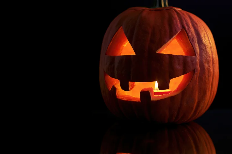 Carved pumpkin glowing from within on a dark reflective surface