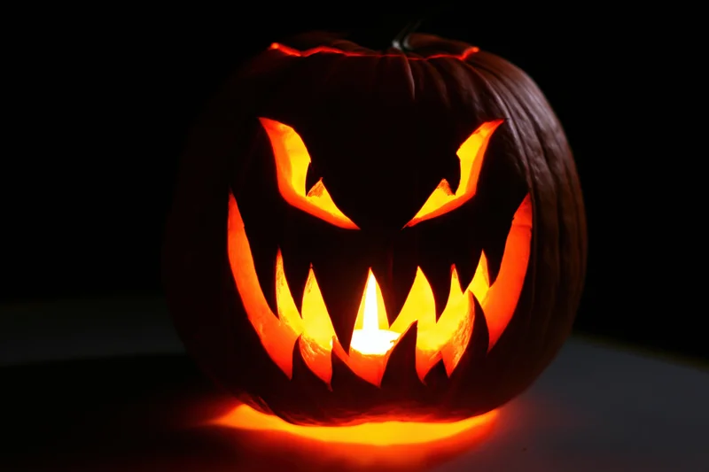 Carved pumpkin with glowing face lit by candle in darkness