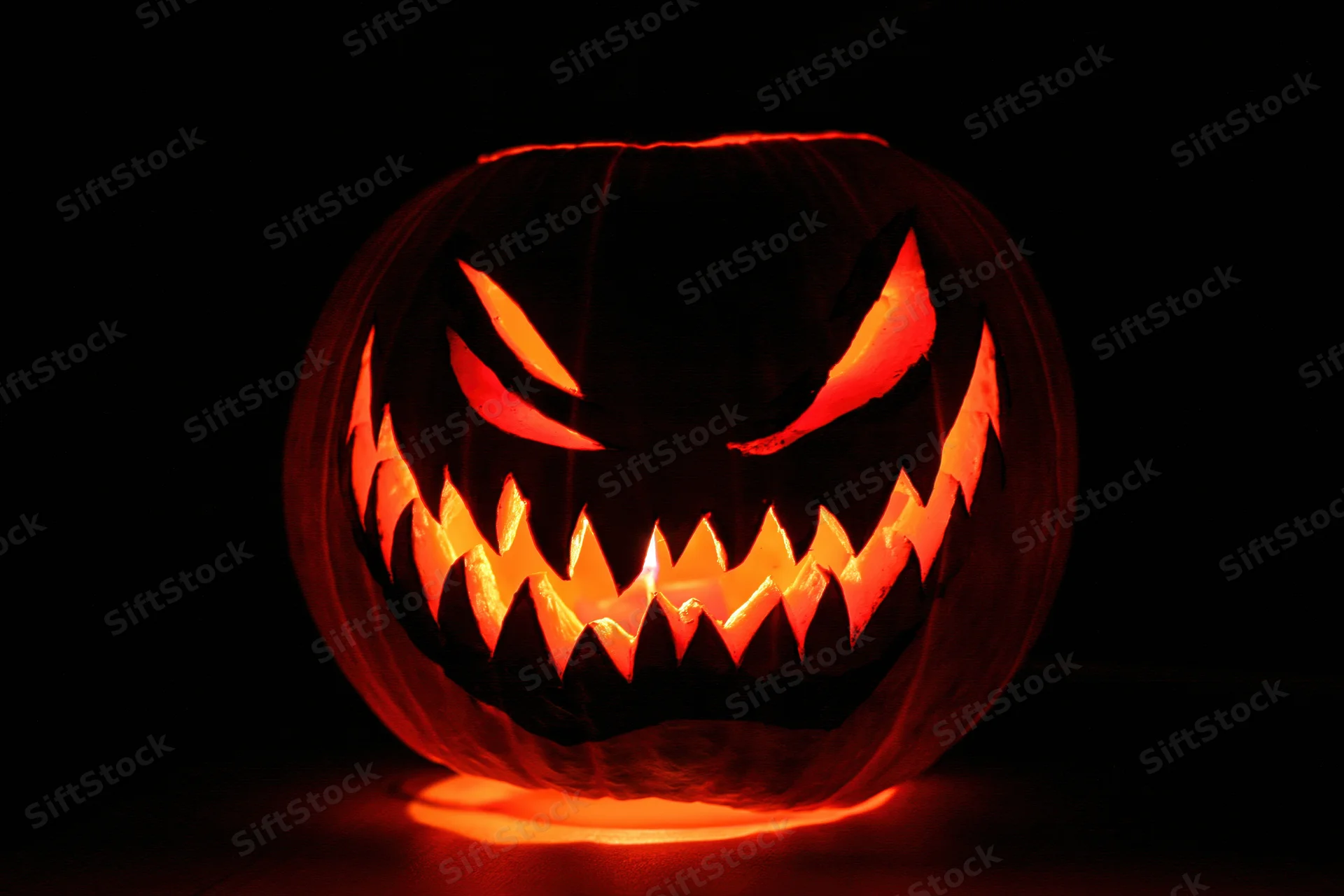 Carved pumpkin with glowing face lit from within in complete darkness