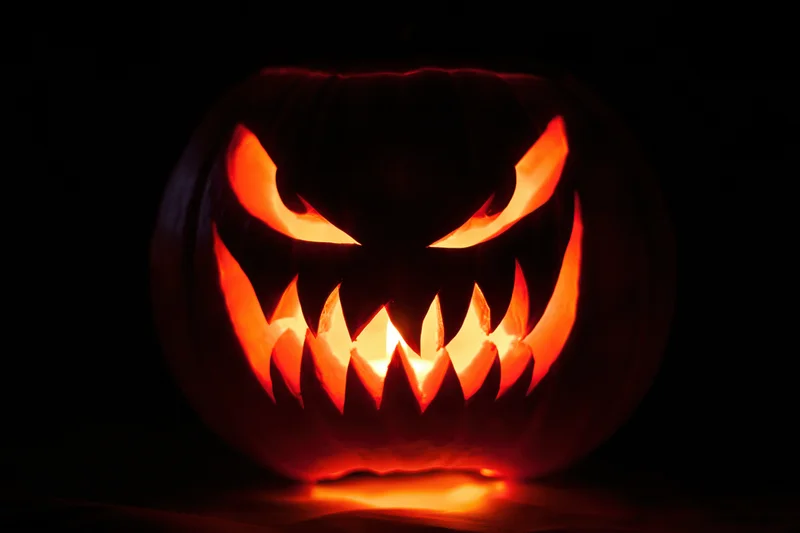 Carved pumpkin with glowing evil face in complete darkness