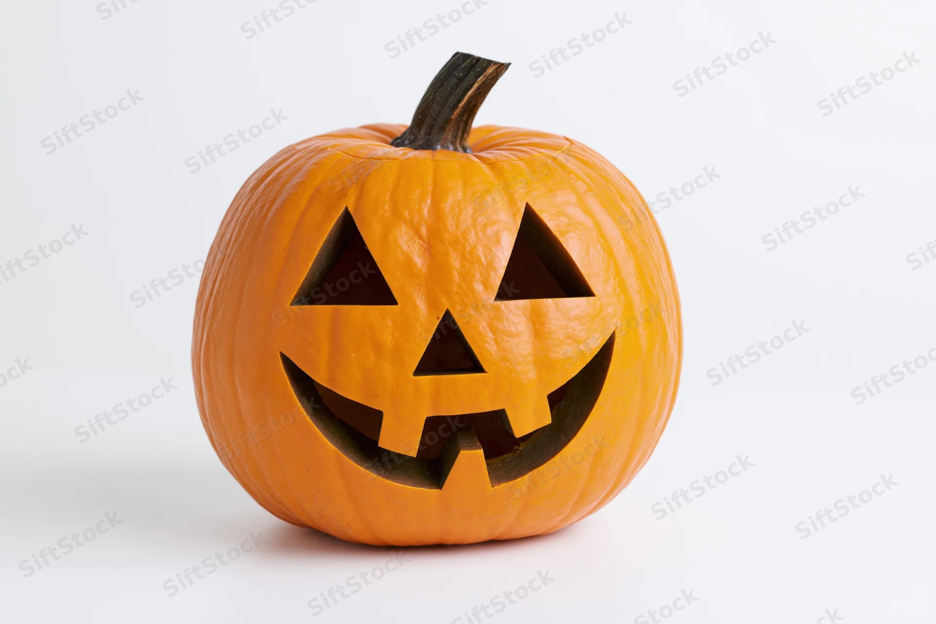 Carved pumpkin with triangular eyes and smiling mouth on white background