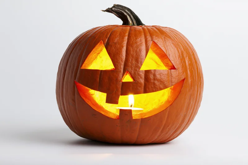 Carved pumpkin with glowing triangular eyes and wide grin lit by candle on white background