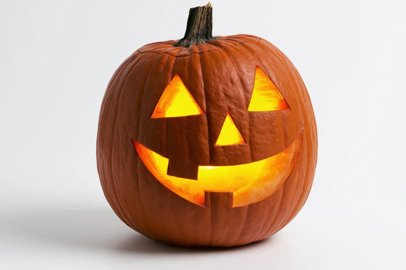 Carved pumpkin with glowing face on white background