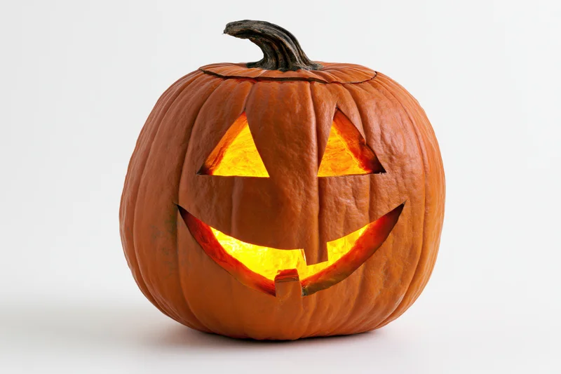 Carved pumpkin with glowing triangular eyes and wide smile on white background
