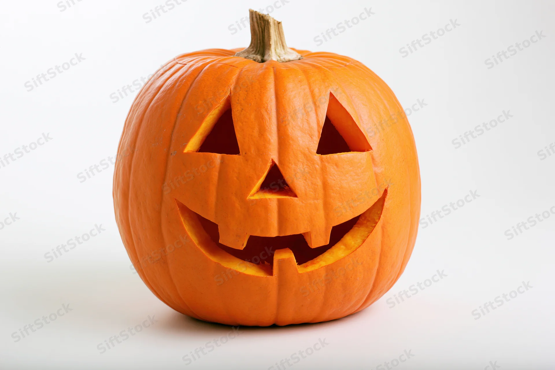 Carved pumpkin with triangular eyes nose and smiling mouth on white background