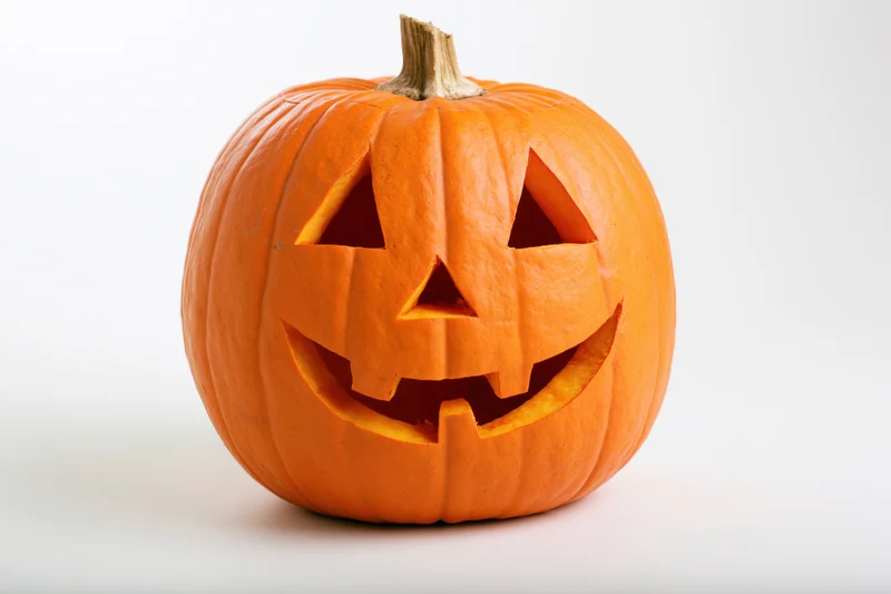 Carved pumpkin with triangular eyes nose and smiling mouth on white background