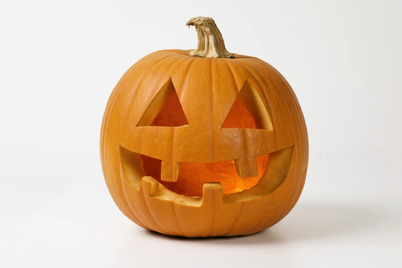 Carved pumpkin with triangular eyes and smiling mouth glowing from within on white background